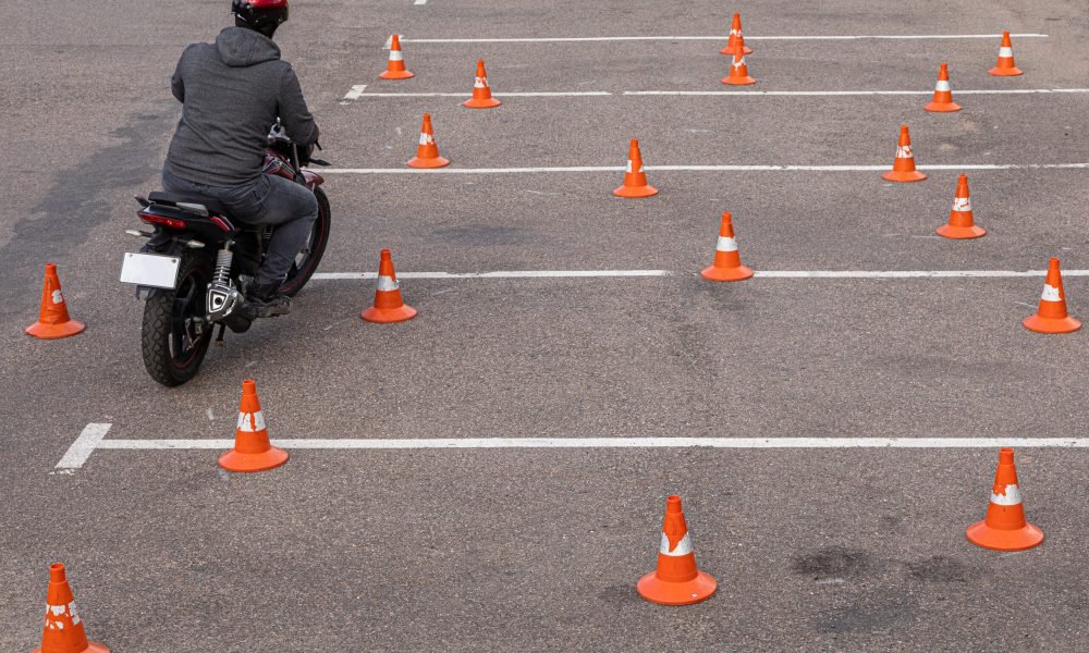 Man in helmet on motor-cycle making exercises on car-park among traffic cones